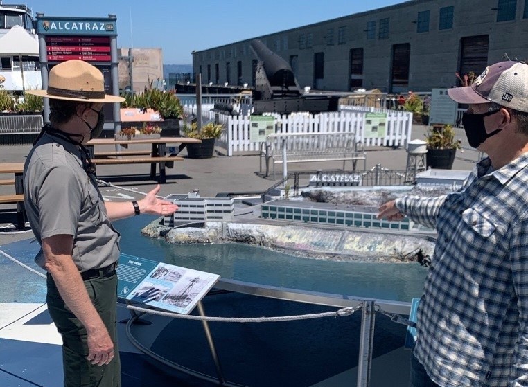 A park ranger gestures toward a model of Alcatraz while talking to a person