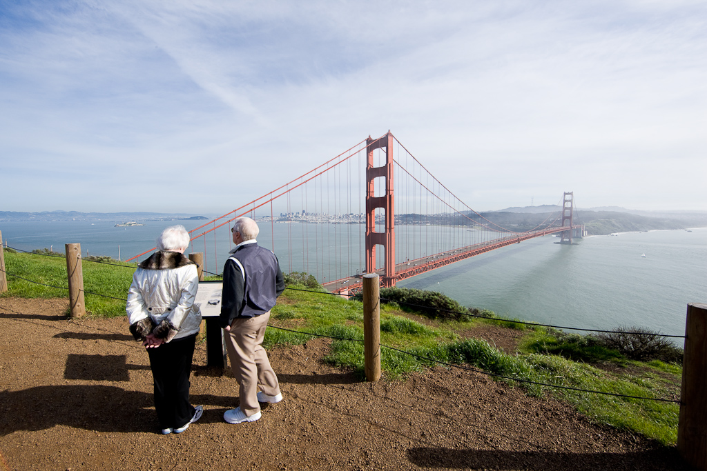 An older couple stands near an interpretive display looking out toward the Golden Gate Bridge and San Francisco.