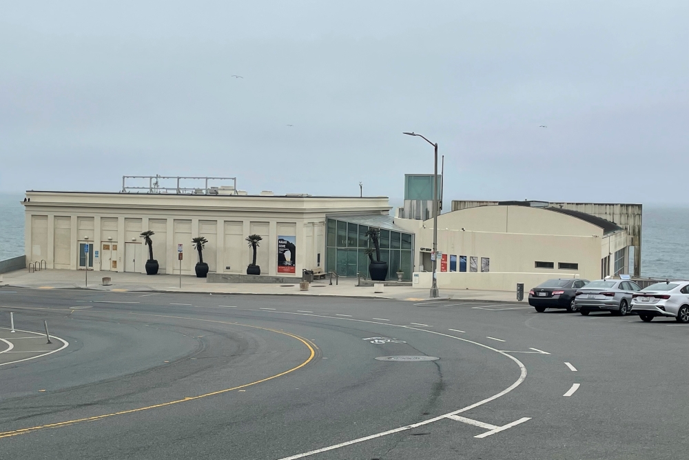 A beige art deco building with a parking lot in front of it