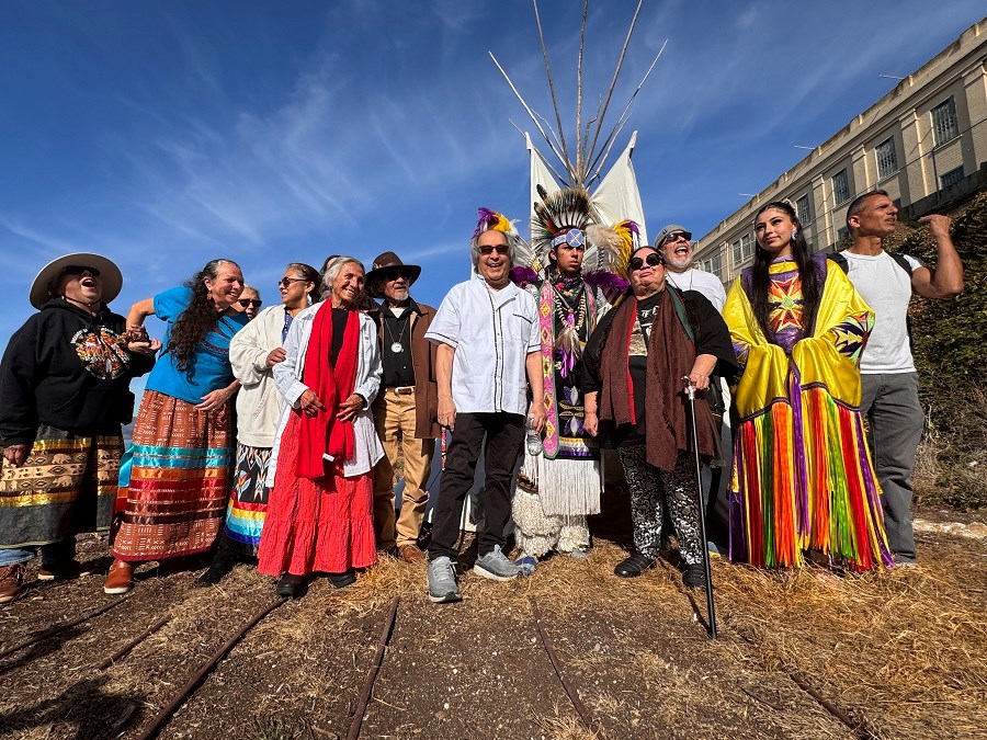 A group of people stand in front of a tipi on Alcatraz Island