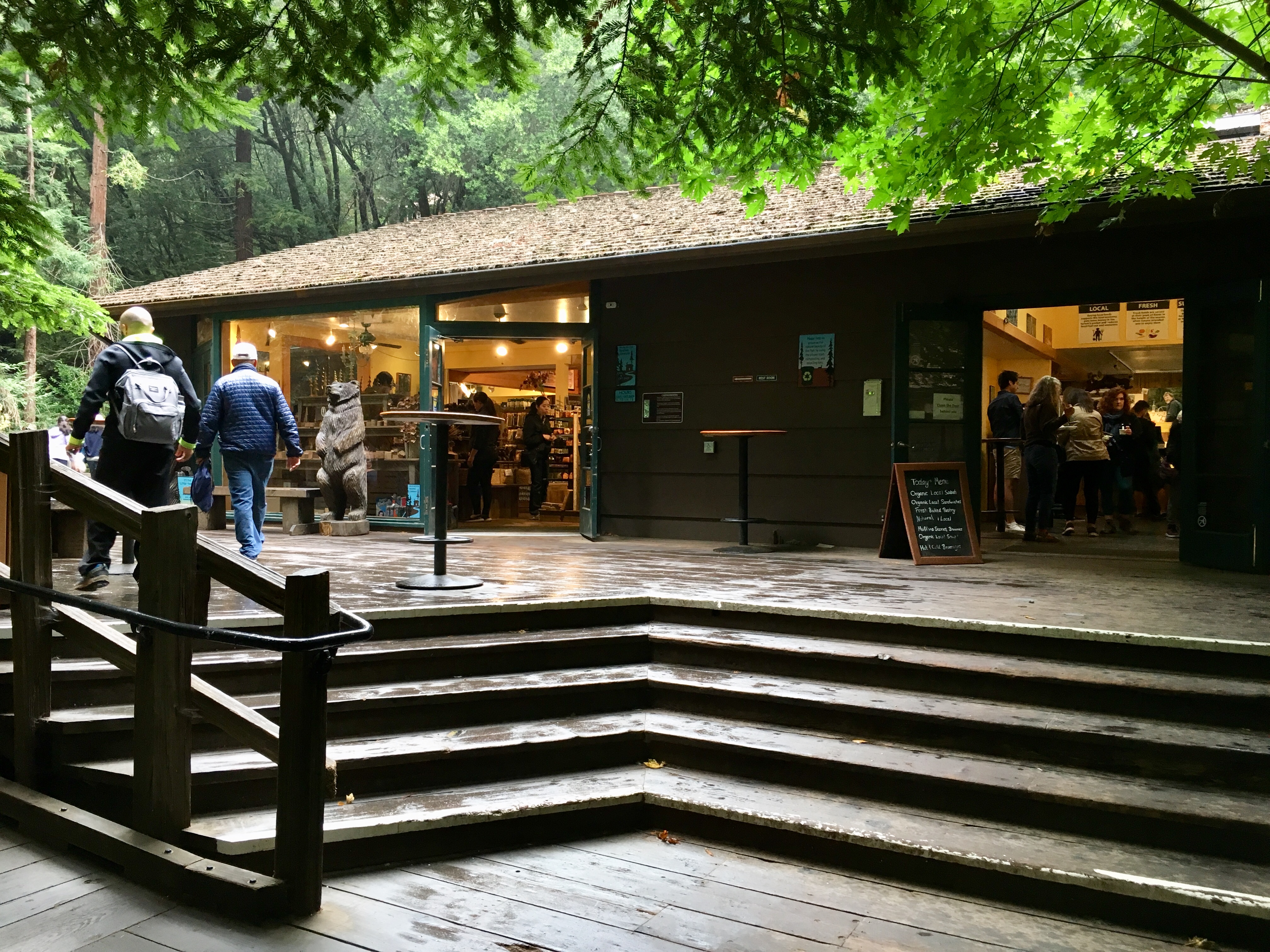 People inside and outside a wooden building with steps leading up to building at Muir Woods National Monument.