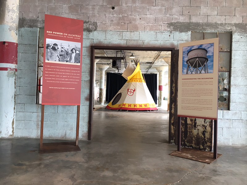 Exhibit panels on each side of doorway with a yellow and white tipi in the next room.