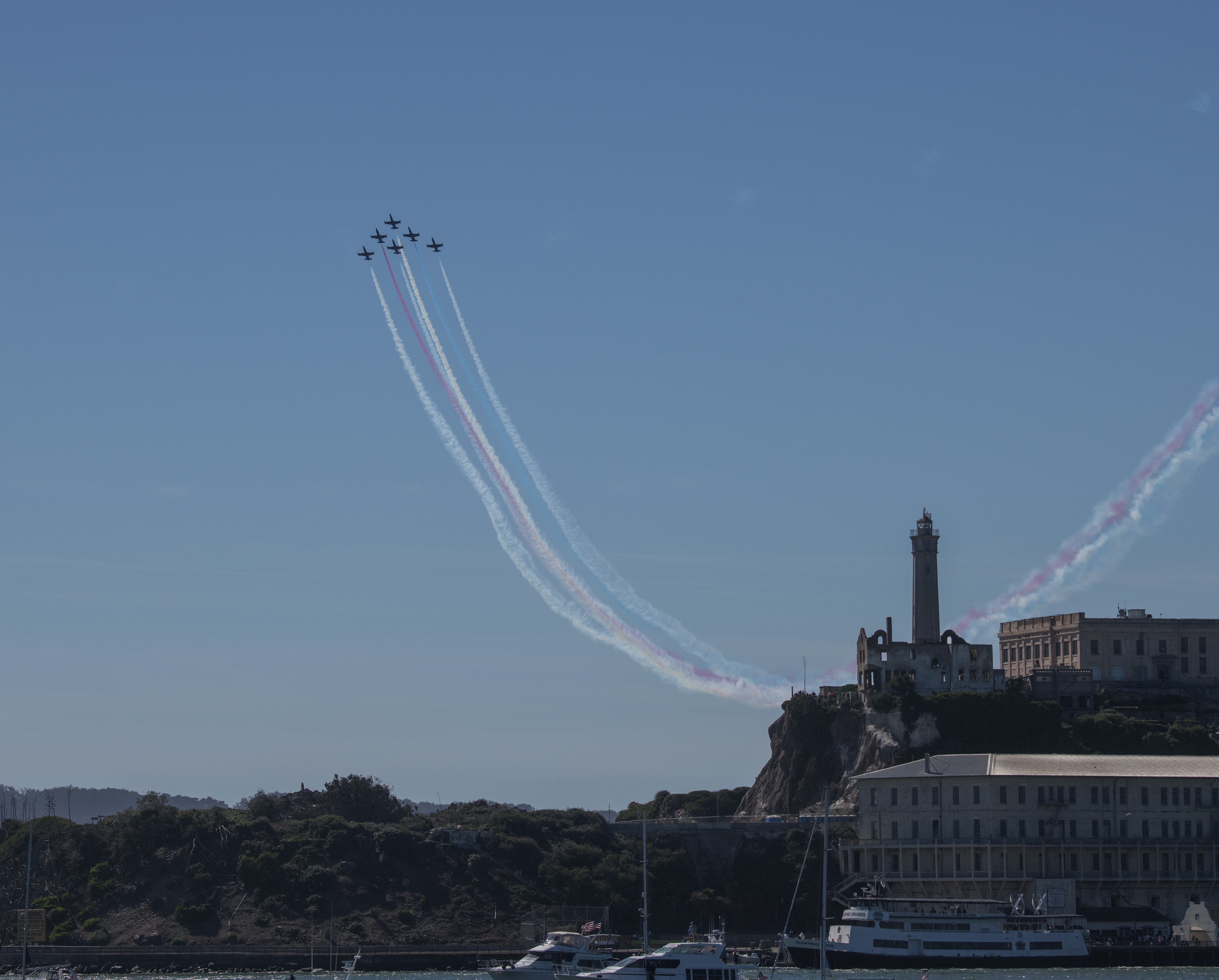 Six Fighter jets in flight together as a triangle trailing three streaks of red, white, and blue in the sky over the San Francisco Bay. Alcatraz Island is to the right. Six Fighter jets in flight together as a triangle trailing three streaks of red, white, and blue in the sky over the San Francisco Bay. Alcatraz Island is to the right.