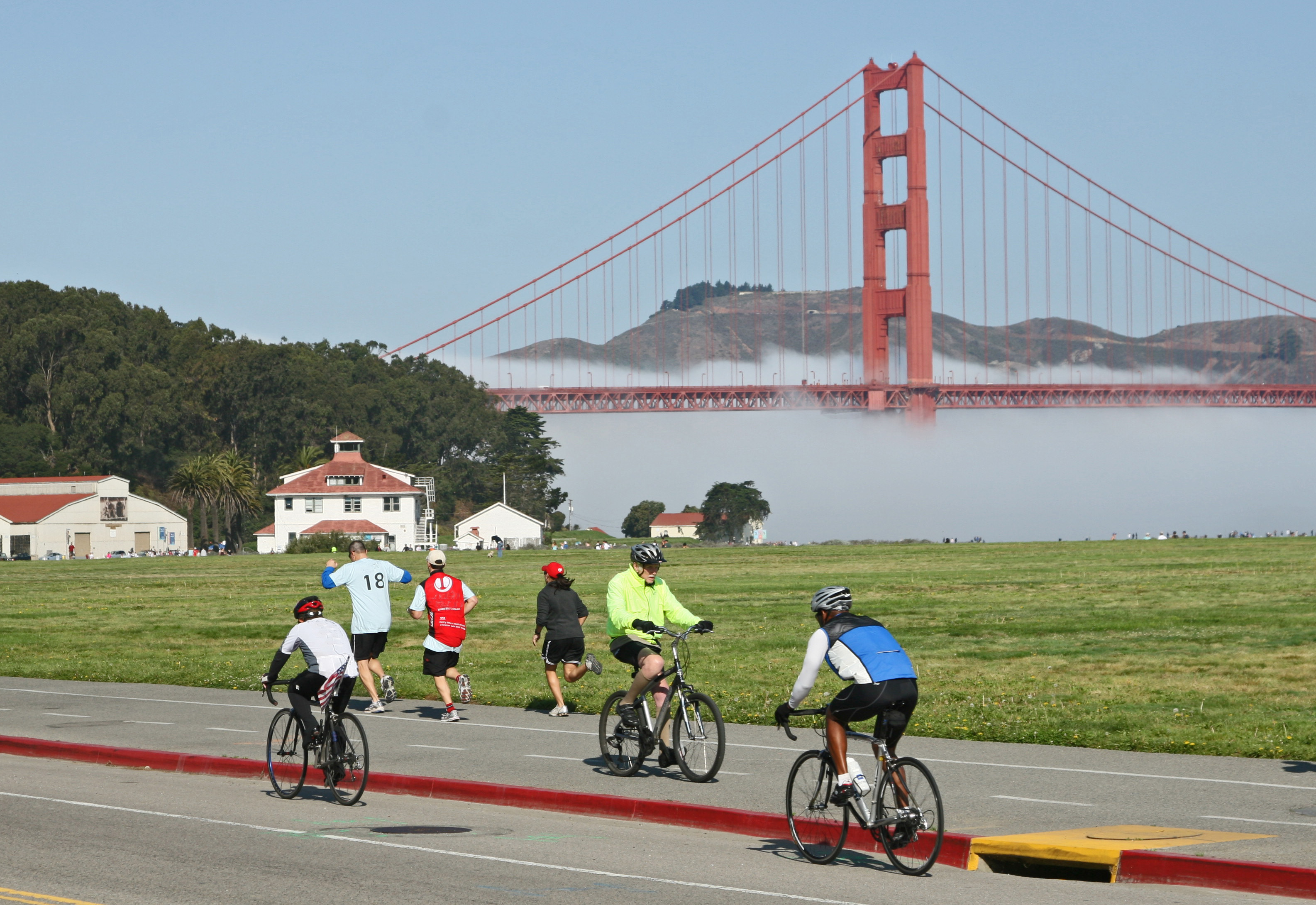 Cyclists and joggers move along Crissy Field as the Golden Gate Bridge stands in the background.