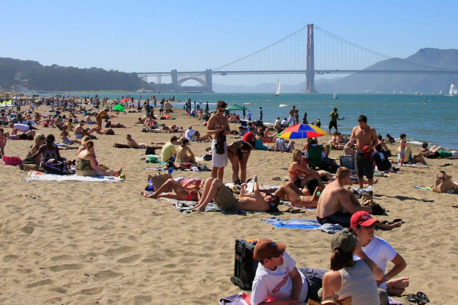 A large group of people at a beach with the Golden Gate Bridge in the distance A large group of people at a beach with the Golden Gate Bridge in the distance