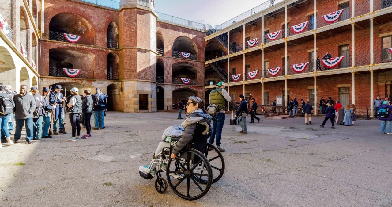 Living History Day at Fort Point Person in wheelchair inside a brick fortress. Men dressed in civil war uniforms stand in the background.