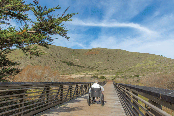 A women in a wheelchair crossing a bridge on the Rodeo Valley Trail. A women in a wheelchair crossing a bridge on the Rodeo Valley Trail.