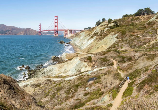 Coastal Trail A trail runs along steep bluffs. A red suspension bridges crosses a strait in the distance