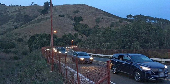 Line of cars on road in twilight with grassy hills behind Line of cars on road in twilight with grassy hills behind