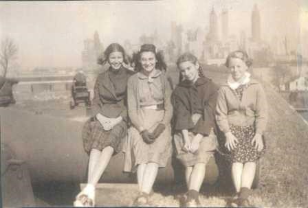 Betty Nickerson and friends sit on a cannon atop Fort Jay with NYC in the background.