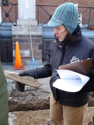 Archaeological Consultant Linda Stone supervised the recent sidewalk construction in the historically sensitive quadrangle in Fort Jay.  Here she observes a piece of slate, probably once used to shingle the roofs in the fort, which was excavated from a fill layer several feet down.