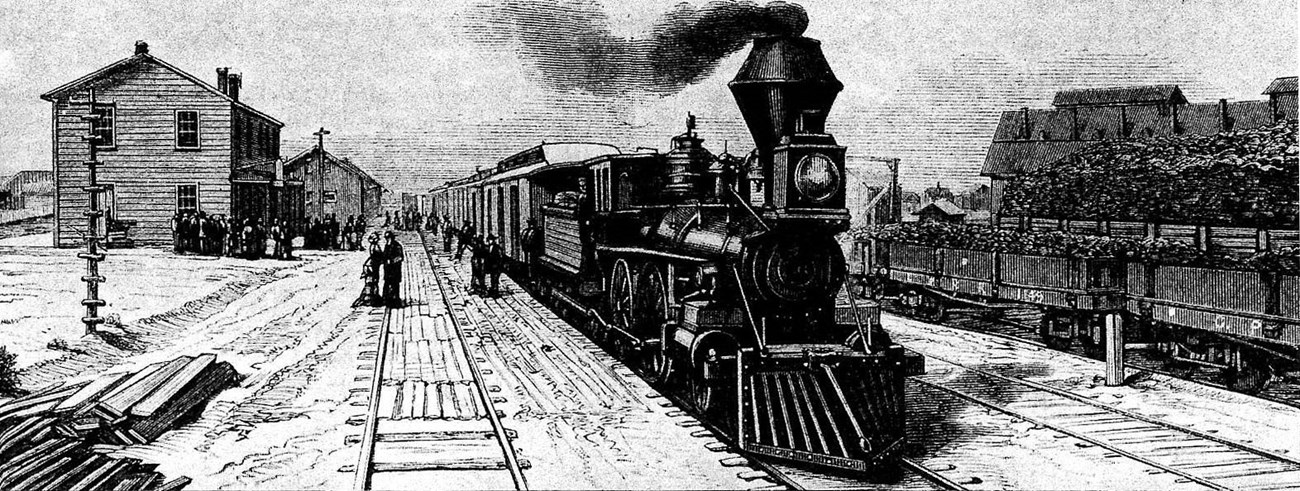 A steam locomotive passes through a primitive train station.