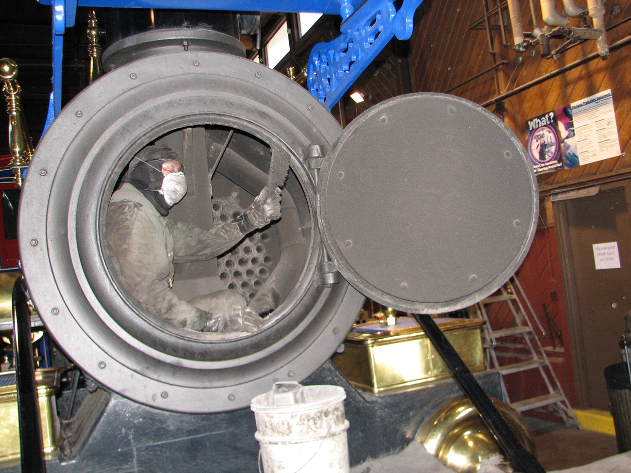 Person sitting inside the Jupiter smokebox, cleaning it with a brush. Boiler tubes can be seen behind him.