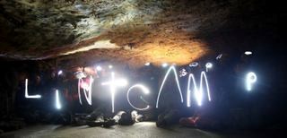 group in cave with flashlight letters spelling out LINT CAMP