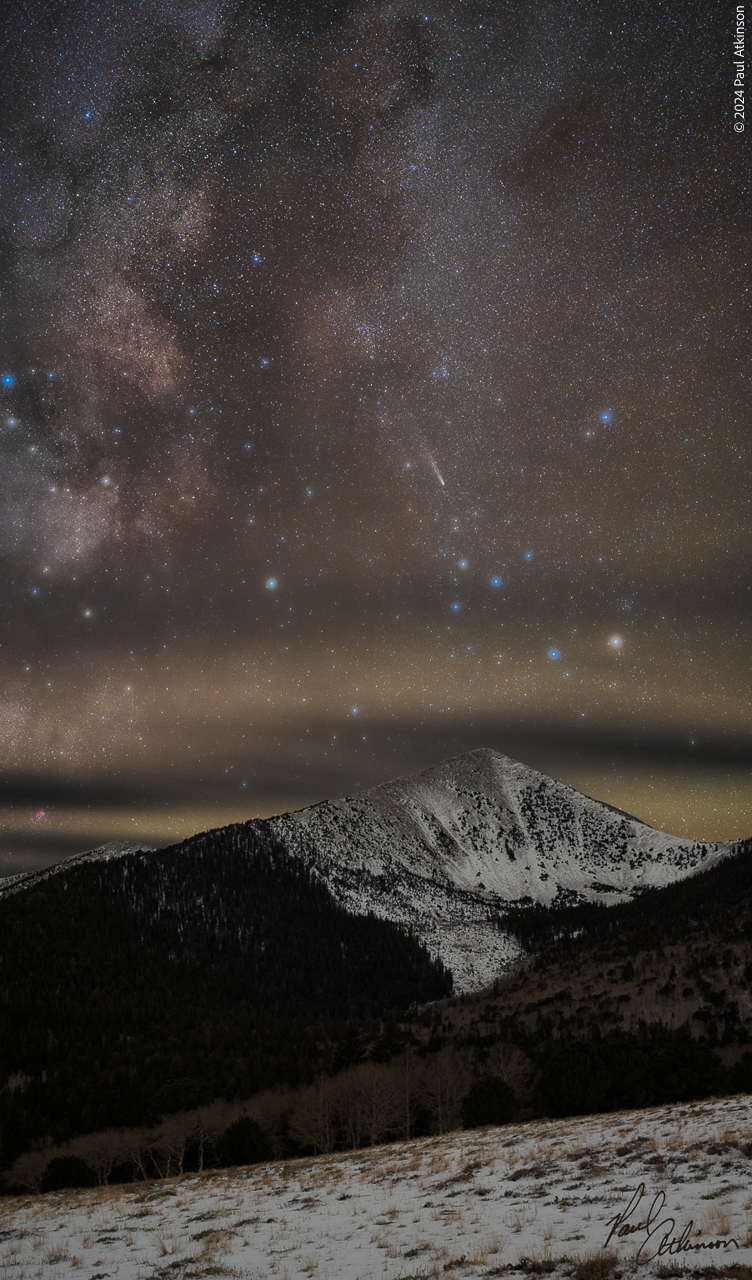 Paul Atkinson - Jewels of the Pyramid A nighttime photo of a snow covered peak with an arcing, colorful milky way above with many bright blue stars shining through the many thousands of smaller white points of light