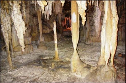 white and tan stalactites, stalagmites and columns in a room within a cave.