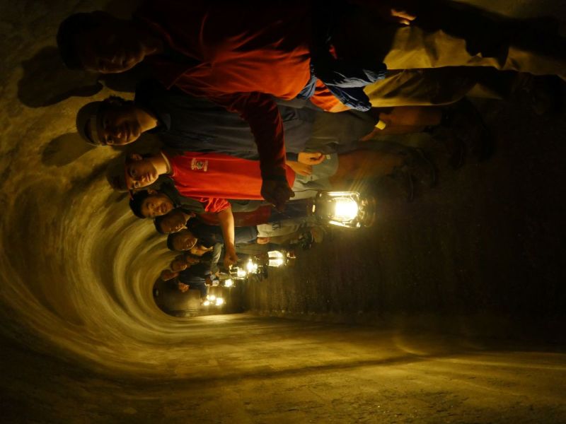 A group of visitors are lined up inside a dark tunnel, illuminated only by electric lanterns they are carrying.