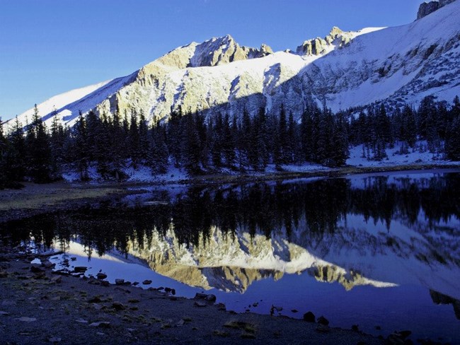 A glassy smooth lake with rugged mountains dusted in snow. A glassy smooth lake with rugged mountains dusted in snow.