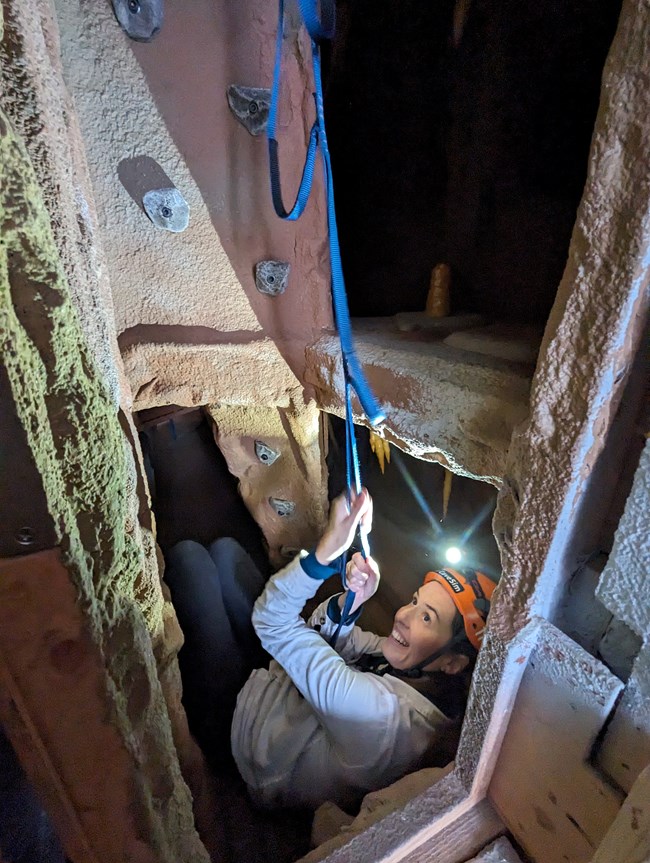 A woman climbs a ladder made of webbing inside a simulated cave passage in Great Basin National Park's CaveSim.