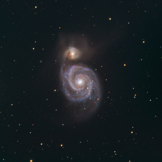 An image of Messier 51a & 51b. These are two interacting galaxies, with one above the other from our perspective. The larger of the two 51a is more blue and below the other more yellow and whispy 51b. The bottom galaxy has a more defined structure.
