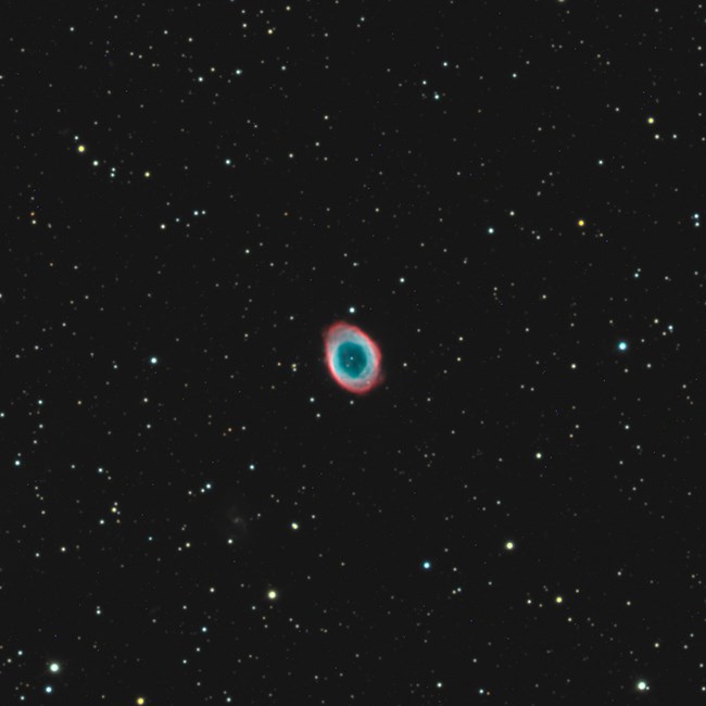 A sea of different stars surrounds the Ring Nebula, a blue/green/red collection of gas and dust in space