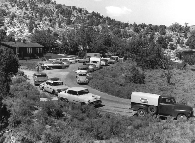 black and white photo of a small visitor center with flagpole and a full parking lot.