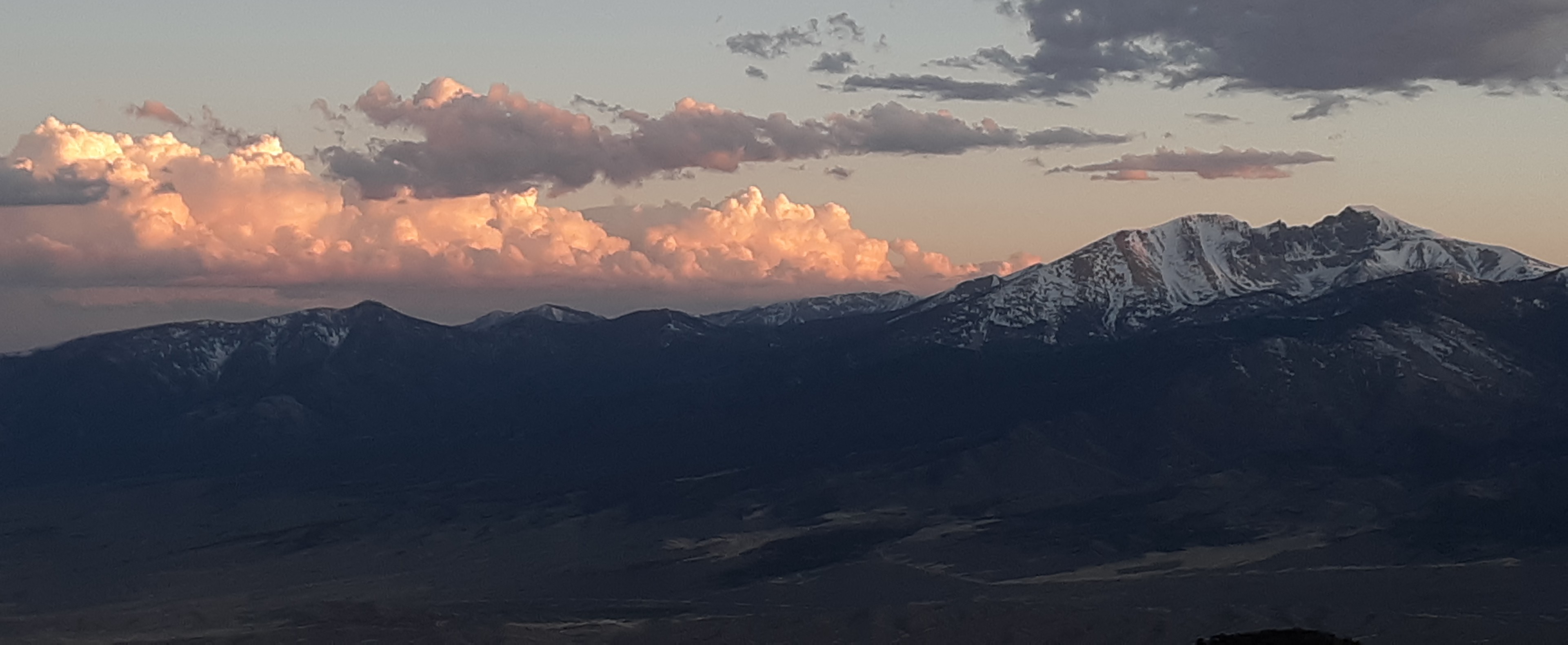 An image of a mountain range at sunset, with the peaks covered in a light layer of snow.