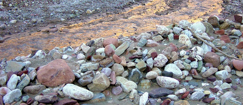 warm light of sunset reflected off a cliff onto a creek with a variety of river cobbles lining the bank.