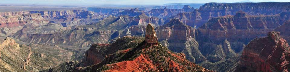 expansive view from Point Imperial showing numerous buttes, peaks and ridgelines within Grand Canyon with the level Painted Desert off in the distance.