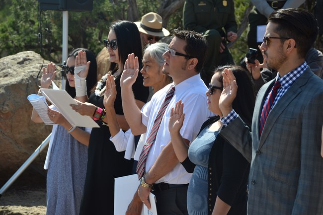 A close up shot of six people as they raise their right hand as they are sworn in as United States Citizens during a naturalization ceremony.