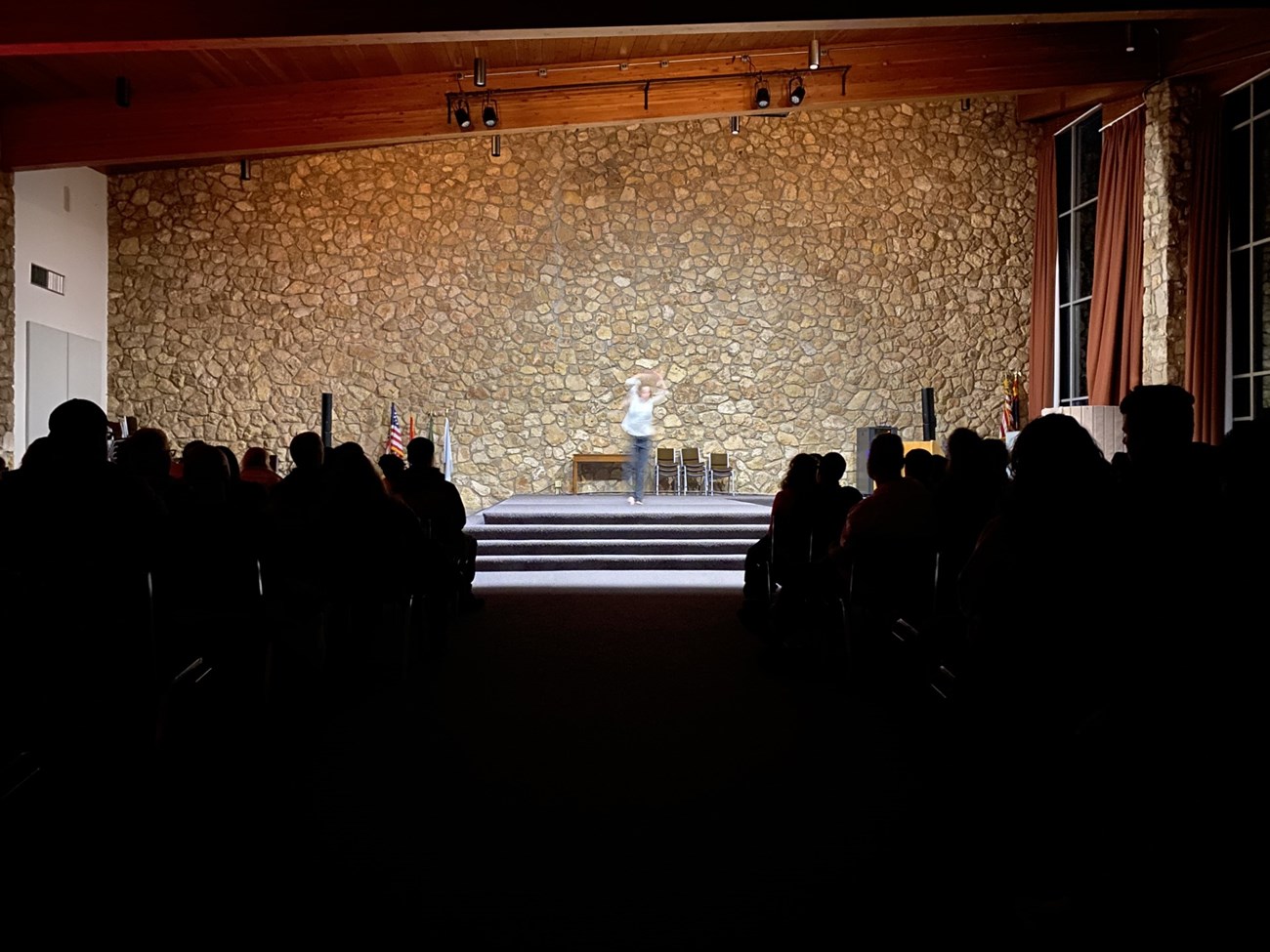 A woman dances under spotlight in front of silhouetted visitors.