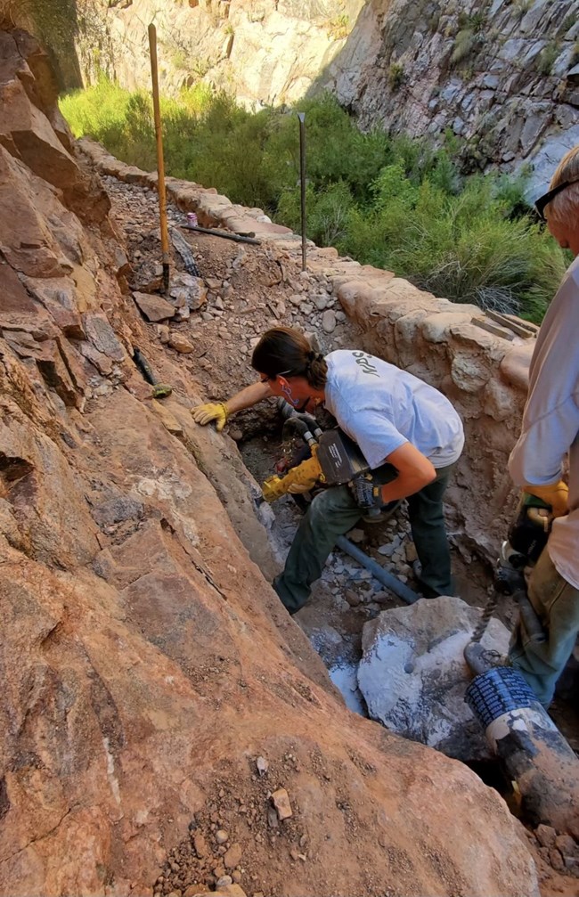 A park staff member uses a jackhammer to create enough clearance around a water pipeline to conduct necessary repairs.