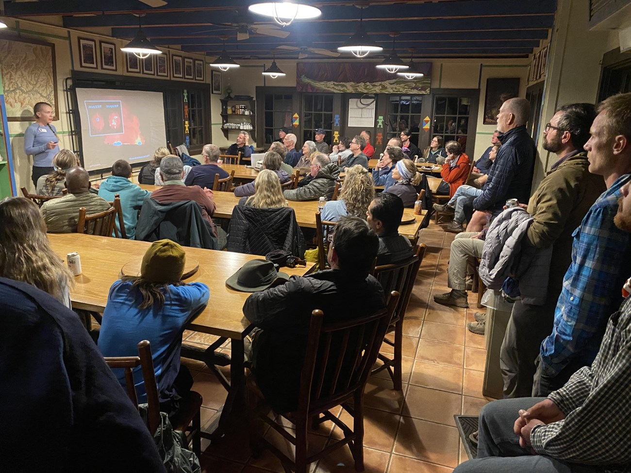 A group of people gathered in a cantina, watching a presentation.