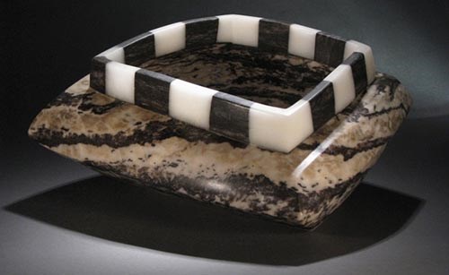 a bowl made out of a highly polished beige rock with black inclusions. The rim of the bowl is a made from a circular strip of alternating black and white alabaster squares.