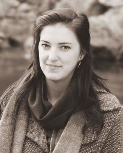 black and white photo of a young woman with long, dark hair and wearing a tweed coat.