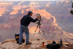 Landscape painter at work at his easel with sunrise on the Grand Canyon walls in the background.
