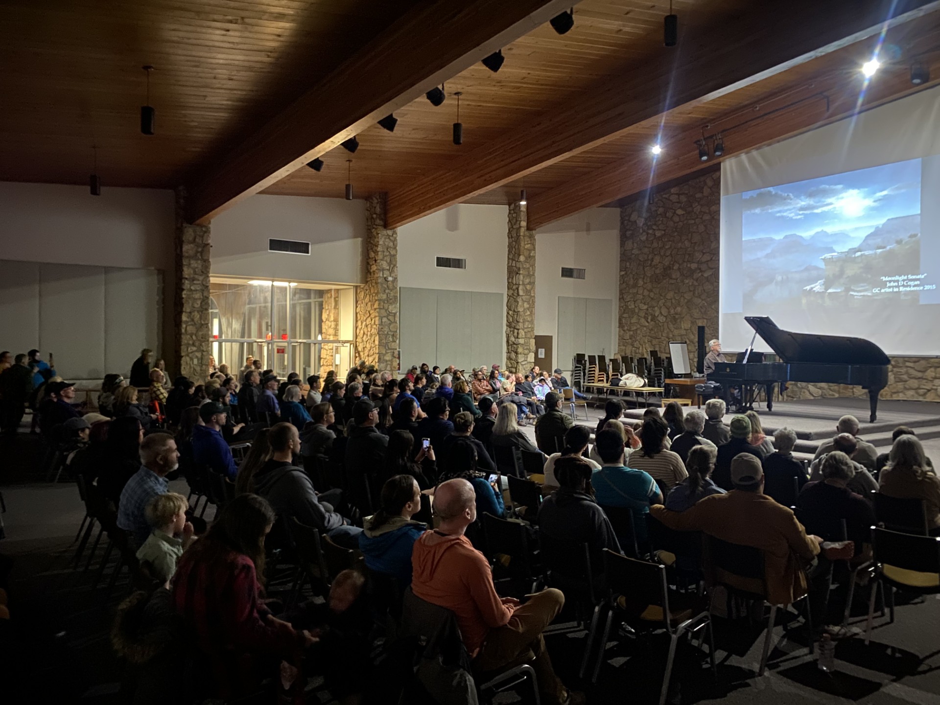 An auditorium filled with people--a Steinway piano on the stage as a man plays.