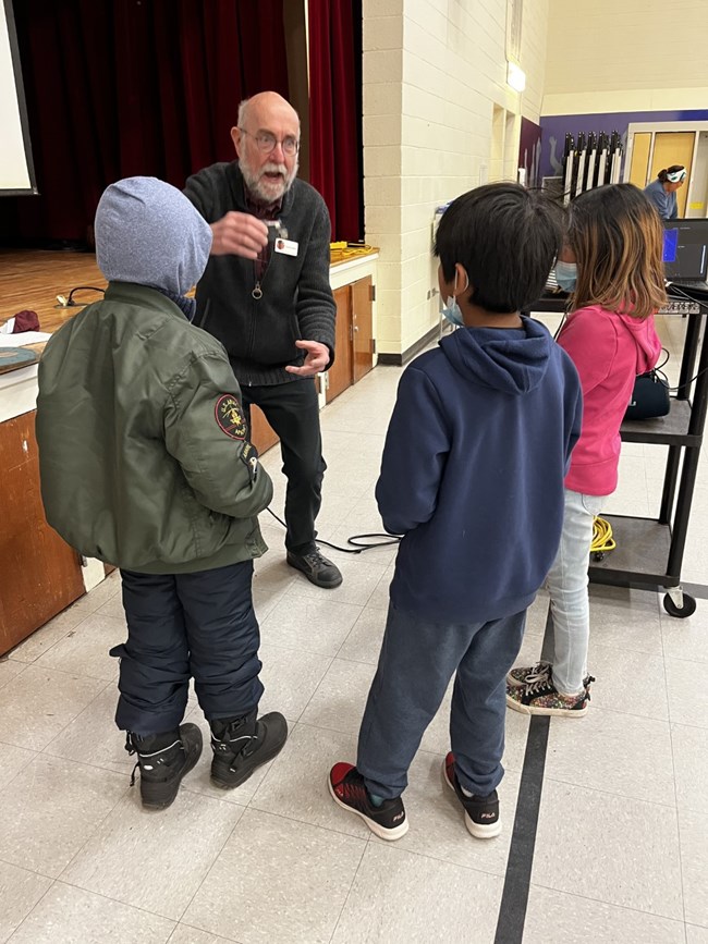 A man explains a concept to eager school children.