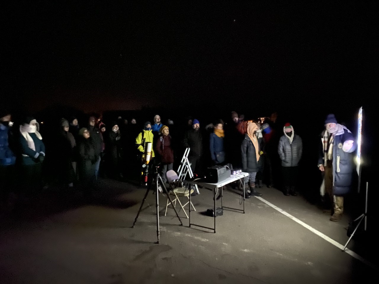 A group of visitors gather around a projector screen outside under the stars.