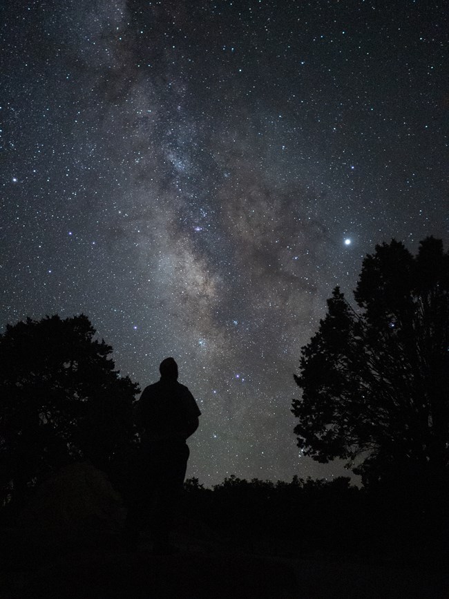 A silhouette stands underneath the Milky Way.