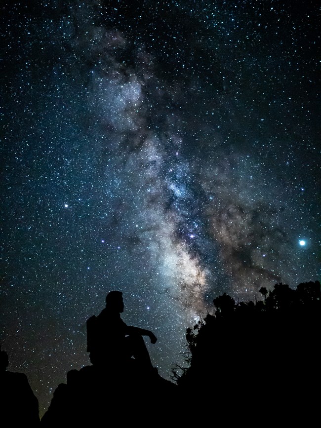 A silhouette of a person sitting in front of the Milky Way.