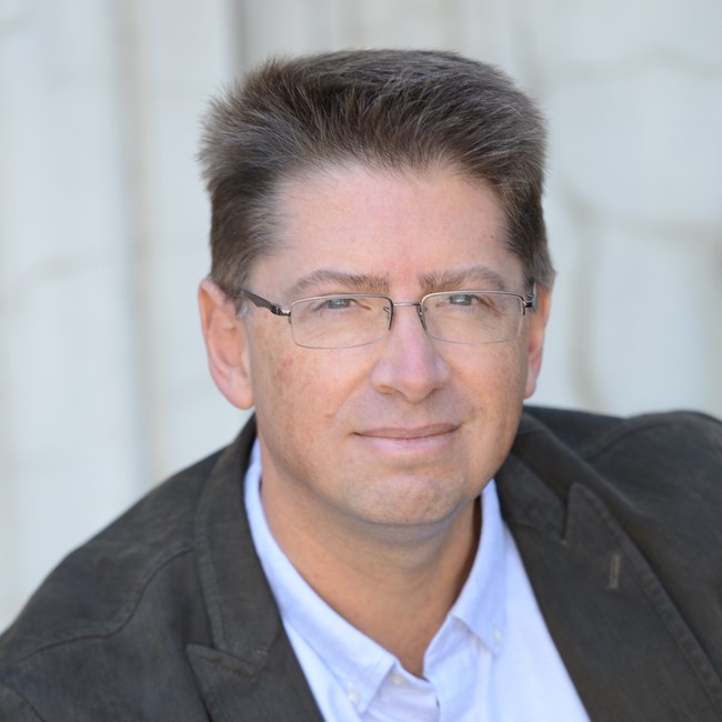 A headshot of a white male with brown hair and glasses.