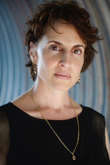 A woman with short brown hair wearing a black blouse and gold necklace.