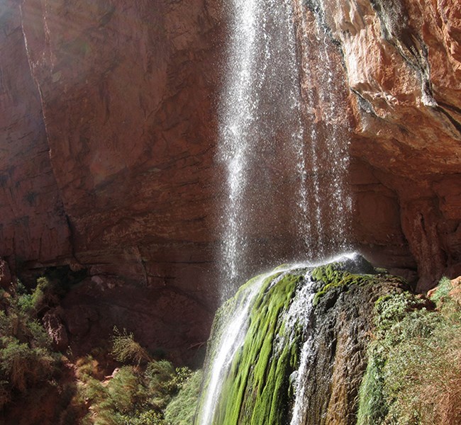 A waterfall descends off a ledge, through midair and lands on a mossy outcropping. The water is slightly blurred.