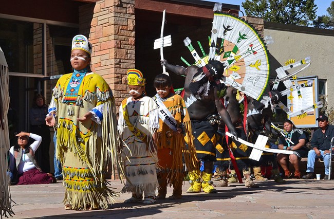 Children stand in a row, ready to dance, dressed in native clothing.