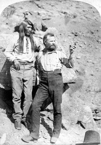 Black and white image of a bearded white man pointing out, next to a Paiute Native American man.