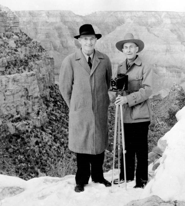 The Kolb Brothers Two brothers holding a tripod stand in front of the snowy canyon