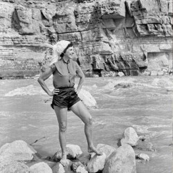 Woman standing on rocks in river with cliff in background