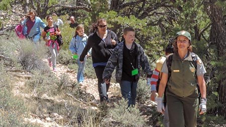 Park ranger leading a family group down an unpaved trail with trees in the background