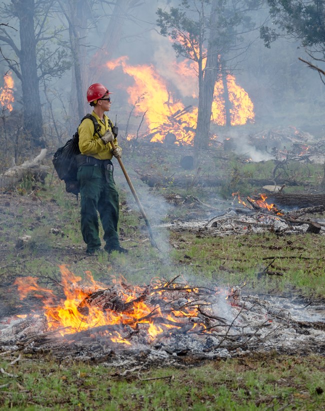 a firefighter watches piles of fuel burning
